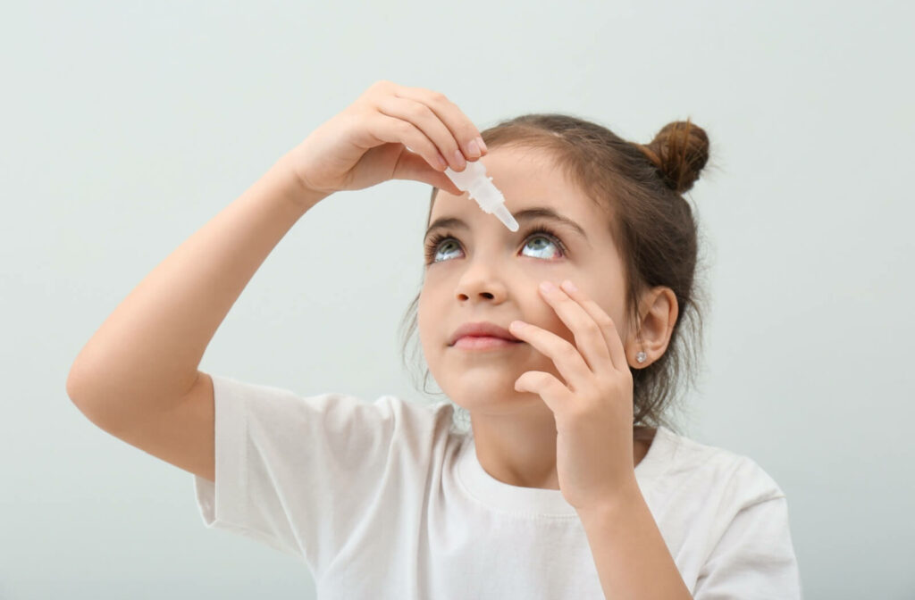 A young girl holds her lower eyelid down as she applies eye drops to her eye to relieve dry eye symptoms