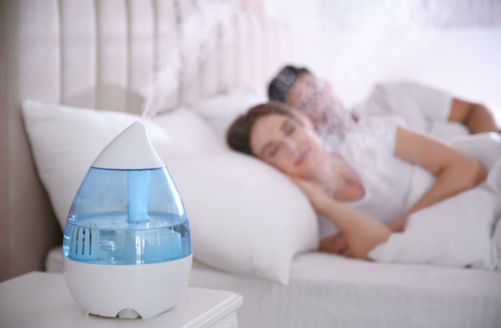 A couple peacefully sleeps in a fresh, all-white bed while a blue humidifier keeps the air hydrated