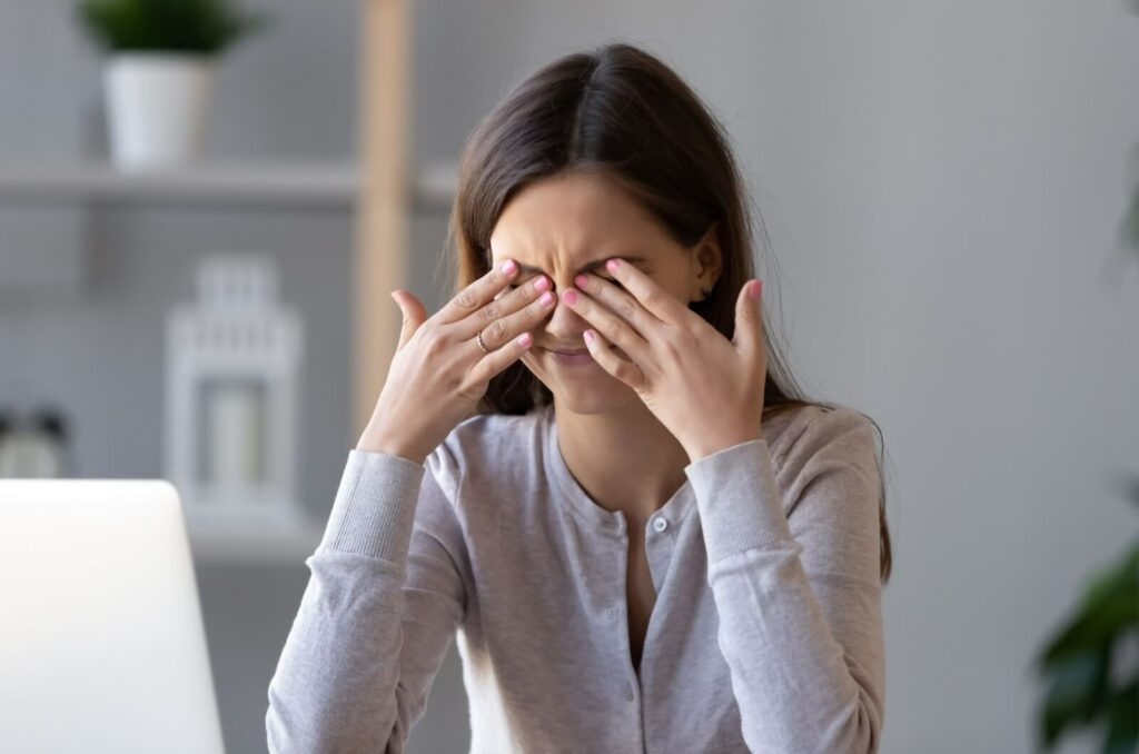 A young adult rubbing their eyes in frustration due to discomfort from meibomian gland dysfunction.