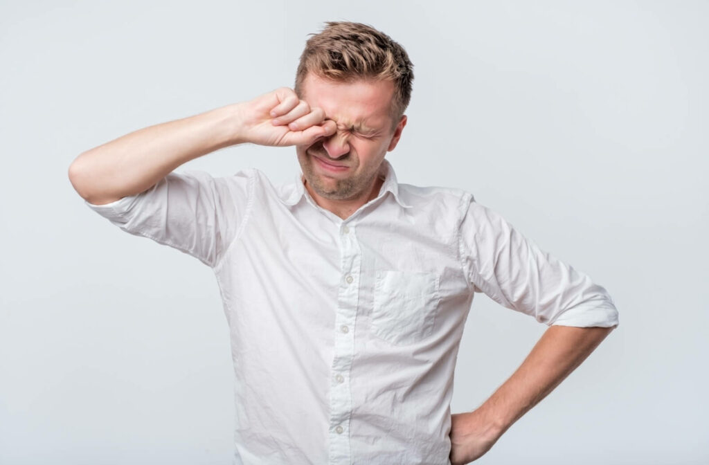 A person rubbing their eyes while appearing uncomfortable, illustrating irritation or fatigue.