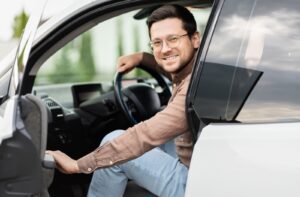 A person smiling as they enter into the driver's seat of a car.