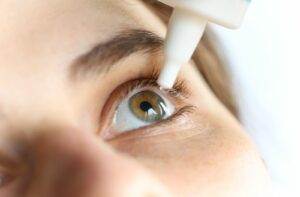 Close-up of eyedropper instilling eyedrop into hazel eye.