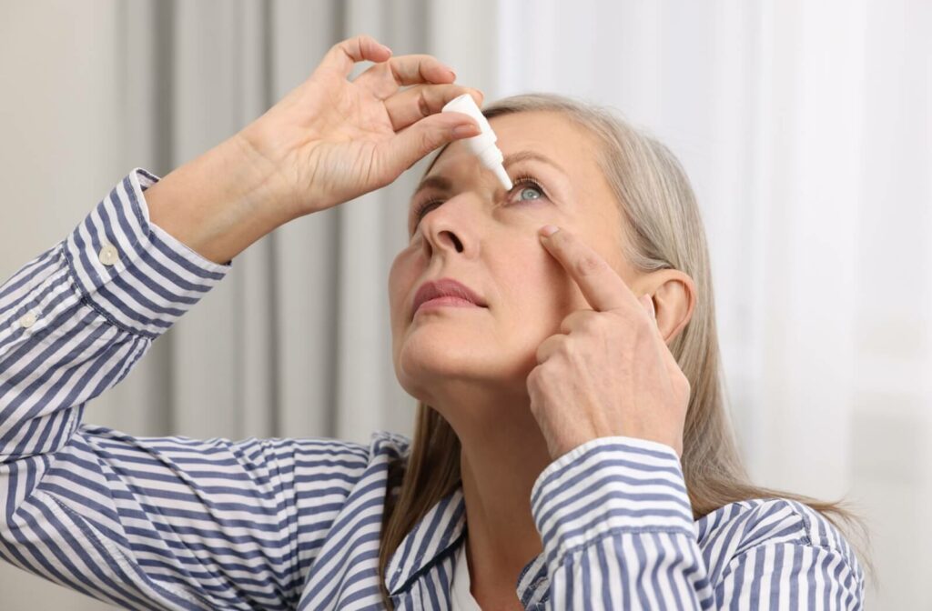 An older person applies eye drops while tilting their head back.