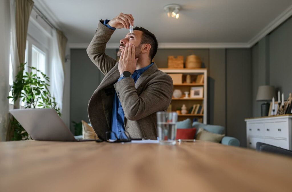 A busy professional puts eye drops in their eyes to help prevent eye strain when spending long hours on their computer.