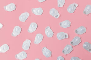 Daily disposable contact lenses in blister packaging are strewn across a bright pink background.