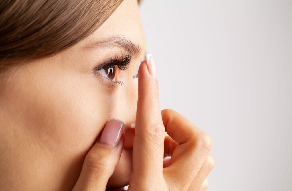 A young adult uses their clean hands to gently place a daily disposable contact lens in their eye.