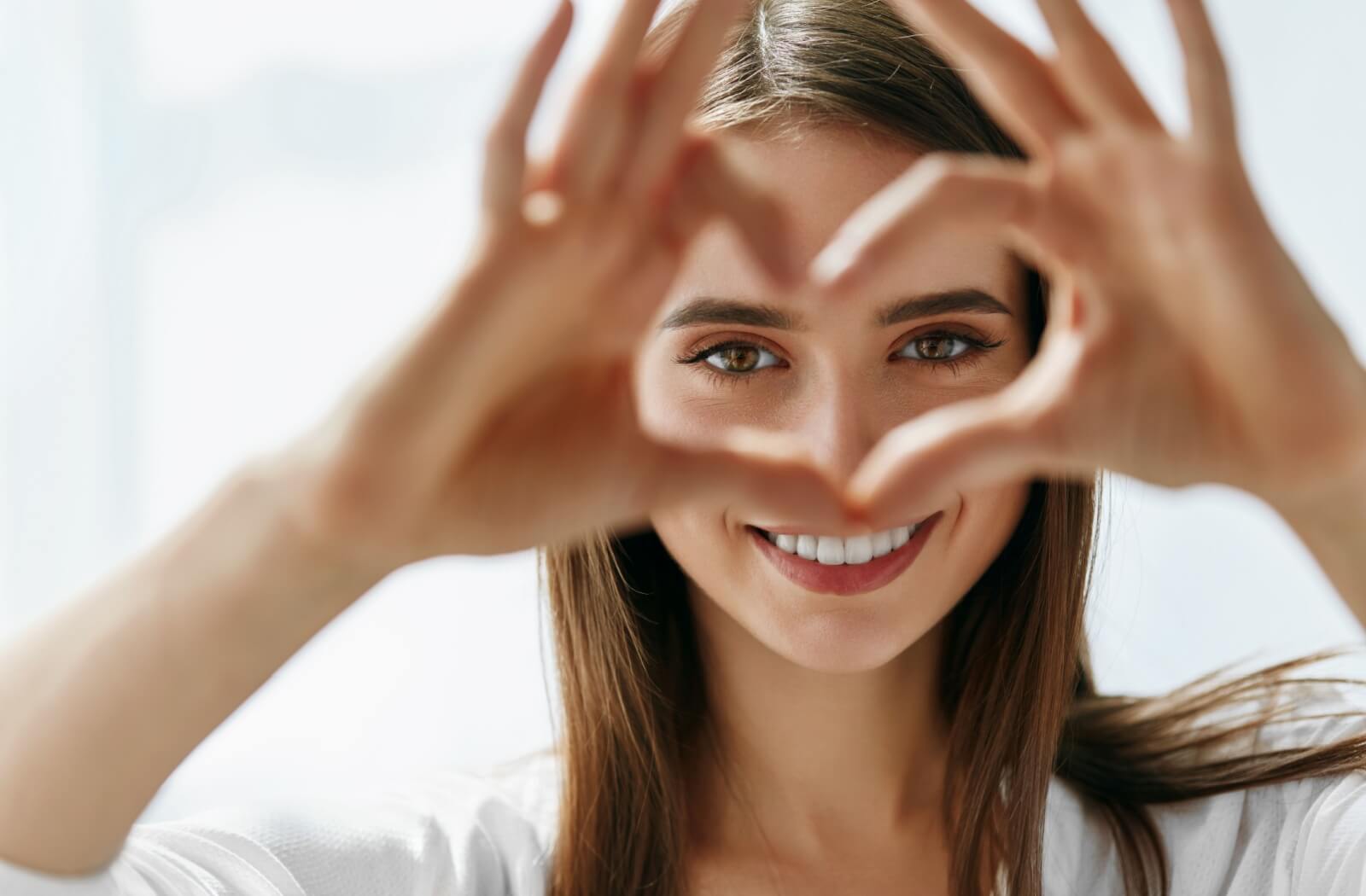 A person smiling and framing their eye with their hands in a heart shape, illustrating healthy vision and eye comfort.