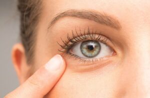 Close-up of an eye with a finger pointing to the fine lines and skin texture underneath.